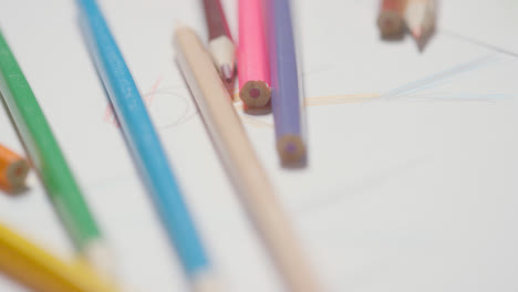 Close-Up-Of-Person-Picking-Up-Multi-Coloured-Pencils-From-Drawings-On-Pad-