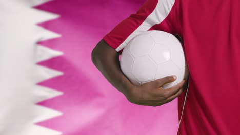 Joven-Futbolista-Caminando-Sosteniendo-El-Fútbol-Frente-A-La-Bandera-De-Qatar