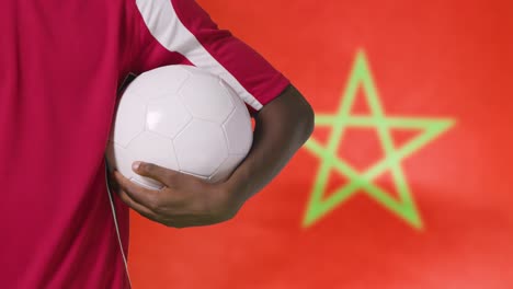 Young-Footballer-Walking-Holding-Football-In-Front-of-Morocco-Flag