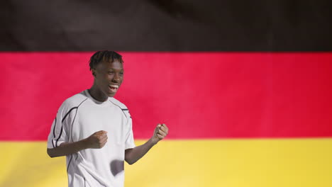 Junger-Fußballer,-Der-Vor-Der-Deutschen-Flagge-Vor-Der-Kamera-Feiert