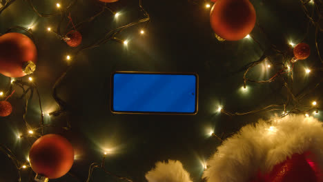 Overhead-Shot-Of-Blue-Screen-Mobile-Phone-With-Christmas-Decorations-Lights-And-Santa-Hat