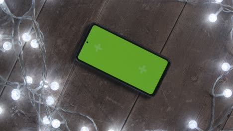 Overhead-Shot-Of-Revolving-Green-Screen-Mobile-Phone-With-Christmas-Decorations-And-Lights-1