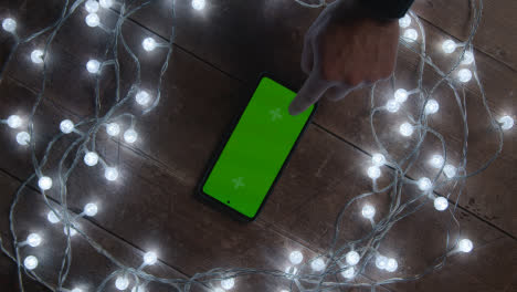 Overhead-Shot-Of-Person-Using-Green-Screen-Mobile-Phone-Surrounded-By-Christmas-Decorations-And-Lights-1