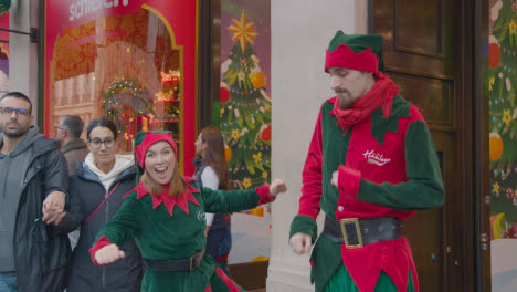 Sales-Assistants-Dressed-As-Elves-With-Shoppers-On-London-UK-Regent-Street-Walking-Past-Hamleys-Toy-Store-Decorated-For-Christmas