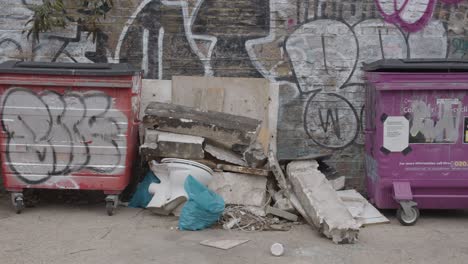 Rubbish-And-Wheelie-Bins-In-Front-Of-Graffiti-Covered-Wall-In-Tower-Hamlets-London-UK