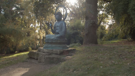 Sculpture-Of-Buddha-In-Arboretum-With-Colourful-Autumn-Trees-In-Background