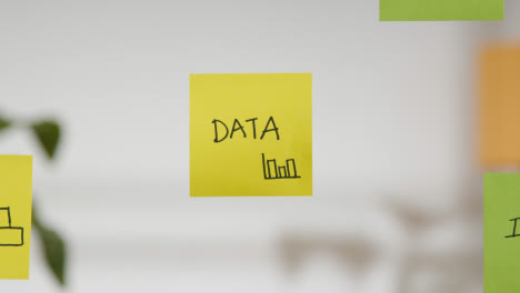 Close-Up-Of-Woman-Putting-Sticky-Note-With-Data-Written-On-It-Onto-Transparent-Screen-In-Office