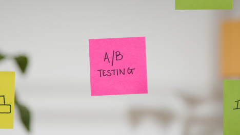 Close-Up-Of-Woman-Putting-Sticky-Note-With-A/B-Testing-Written-On-It-Onto-Transparent-Screen-In-Office