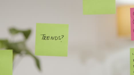 Close-Up-Of-Woman-Putting-Sticky-Note-With-Trends-Written-On-It-Onto-Transparent-Screen-In-Office-1