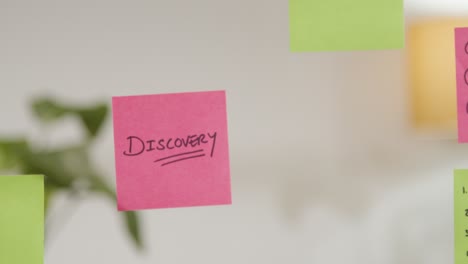 Close-Up-Of-Woman-Putting-Sticky-Note-With-Discovery-Written-On-It-Onto-Transparent-Screen-In-Office-