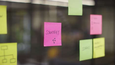 Close-Up-Of-Woman-Putting-Sticky-Note-With-Strategy-Written-On-It-Onto-Transparent-Screen-In-Office-1
