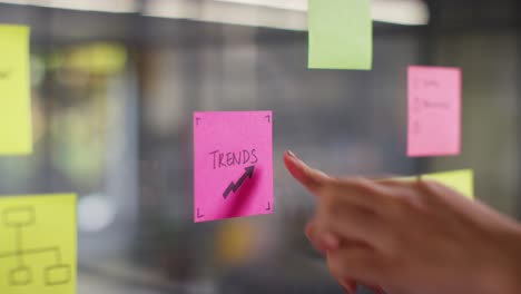 Close-Up-Of-Woman-Putting-Sticky-Note-With-Trends-Written-On-It-Onto-Transparent-Screen-In-Office-1