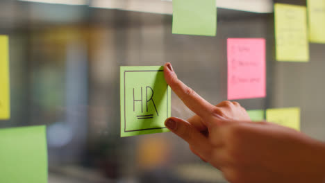 Close-Up-Of-Woman-Putting-Sticky-Note-With-HR-Written-On-It-Onto-Transparent-Screen-In-Office-2