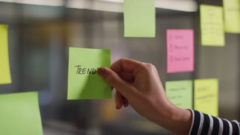 Close-Up-Of-Woman-Putting-Sticky-Note-With-Trends-Written-On-It-Onto-Transparent-Screen-In-Office-2