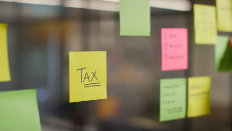 Close-Up-Of-Woman-Putting-Sticky-Note-With-Tax-Written-On-It-Onto-Transparent-Screen-In-Office-1