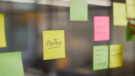 Close-Up-Of-Woman-Putting-Sticky-Note-With-Fintech-Written-On-It-Onto-Transparent-Screen-In-Office-1