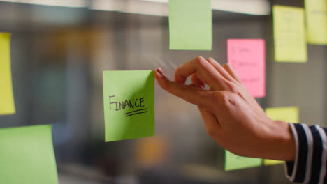 Close-Up-Of-Woman-Putting-Sticky-Note-With-Finance-Written-On-It-Onto-Transparent-Screen-In-Office-1