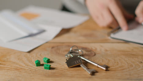 Hauskaufkonzept-Mit-Schlüsseln-Am-Hausförmigen-Schlüsselring-Und-Person,-Die-Finanzen-überprüft-8
