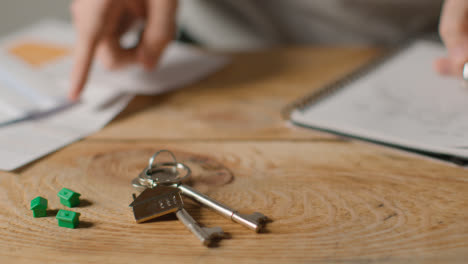 Hauskaufkonzept-Mit-Schlüsseln-Am-Hausförmigen-Schlüsselring-Und-Person,-Die-Finanzen-überprüft-9