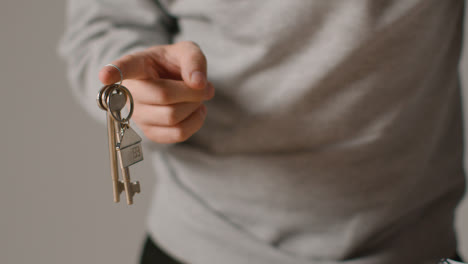 Hauskaufkonzept-Mit-Person,-Die-Schlüssel-Auf-Hausförmigem-Schlüsselring-Vor-Grauem-Hintergrund-Hält