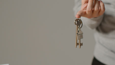 Hauskaufkonzept-Mit-Person,-Die-Schlüssel-Auf-Hausförmigem-Schlüsselring-Vor-Grauem-Hintergrund-Hält-1