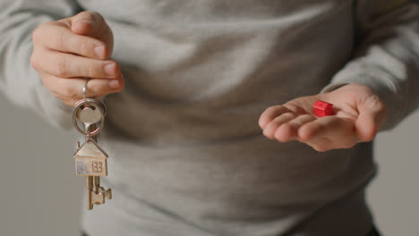 Hauskaufkonzept-Mit-Person,-Die-Schlüssel-Auf-Hausförmigem-Schlüsselring-Und-Rotem-Musterhaus-Hält