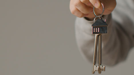 Hauskaufkonzept-Mit-Person,-Die-Schlüssel-Auf-Hausförmigem-Schlüsselring-Vor-Grauem-Hintergrund-Hält-3