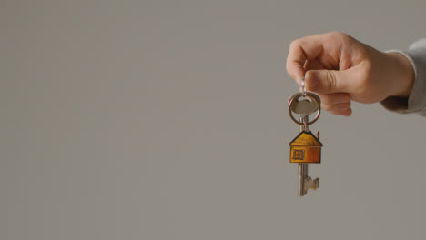 Hauskaufkonzept-Mit-Person,-Die-Schlüssel-Auf-Hausförmigem-Schlüsselring-Vor-Grauem-Hintergrund-Hält-6