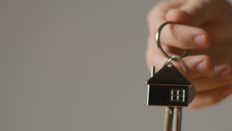 Hauskaufkonzept-Mit-Nahaufnahme-Einer-Person,-Die-Schlüssel-An-Einem-Hausförmigen-Schlüsselring-Vor-Grauem-Hintergrund-Hält-7