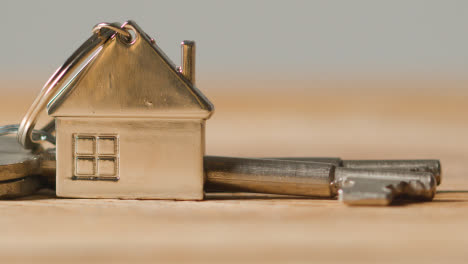 Home-Buying-Concept-With-Close-Up-Of-Keys-On-House-Shaped-Keyring-On-Wooden-Surface