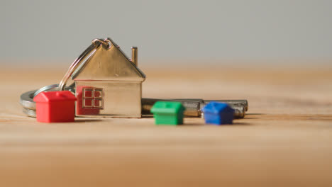Home-Buying-Concept-With-Close-Up-Of-Keys-On-House-Shaped-Keyring-And-Plastic-Houses-On-Wooden-Surface