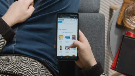 Overhead-Shot-Of-Person-At-Home-Shopping-Online-Looking-At-Costco-Website-On-Mobile-Phone-1