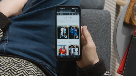 Overhead-Shot-Of-Person-At-Home-Shopping-Online-Looking-At-Asos-Website-On-Mobile-Phone-1
