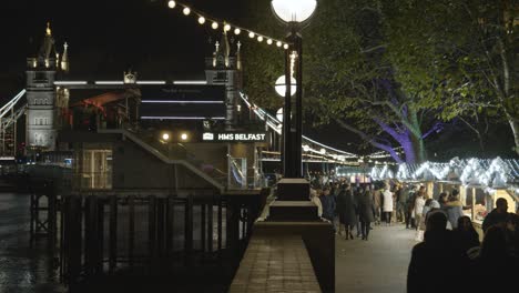 Geschäftige-Weihnachtsmarktstände-Mit-Blick-Auf-Die-Tower-Bridge-Am-Londoner-Südufer-Bei-Nacht