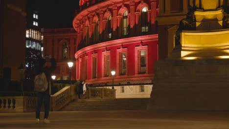Person-With-Phone-Taking-Picture-Of-Exterior-Of-The-Royal-Albert-Hall-in-London-UK-Floodlit-At-Night