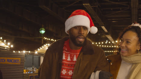 Couple-Celebrating-Christmas-Walking-Through-Market-Stalls-On-London-South-Bank-At-Night-1