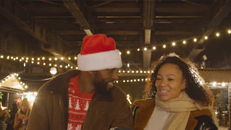 Couple-Celebrating-Christmas-Walking-Through-Market-Stalls-On-London-South-Bank-At-Night-2