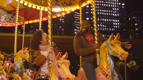 Couple-Having-Fun-Riding-On-Fairground-Roundabout-On-London-South-Bank-At-Night-
