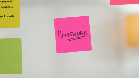 Close-Up-Of-Woman-Putting-Sticky-Note-With-Homework-Written-On-It-Onto-Transparent-Screen-In-Office