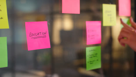 Close-Up-Of-Woman-Putting-Sticky-Note-With-Education-Written-On-It-Onto-Transparent-Screen-In-Office-2