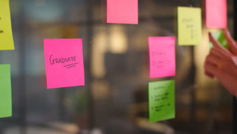 Close-Up-Of-Woman-Putting-Sticky-Note-With-Graduate-Written-On-It-Onto-Transparent-Screen-In-Office-2
