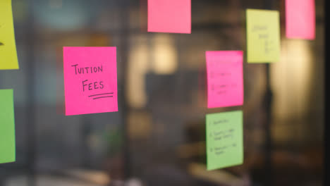 Close-Up-Of-Woman-Putting-Sticky-Note-With-Tuition-Fees-Written-On-It-Onto-Transparent-Screen-In-Office-1