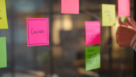 Close-Up-Of-Woman-Putting-Sticky-Note-With-College-Written-On-It-Onto-Transparent-Screen-In-Office-2