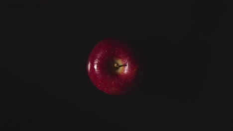 Overhead-Studio-Shot-Of-Hand-Picking-Red-Apple-Revolving-Against-Black-Background