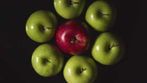 Overhead-Studio-Shot-Of-Red-Apple-In-Circle-Of-Green-Apples-Revolving-Against-Black-Background