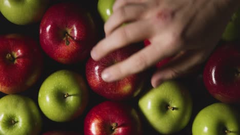 Overhead-Studio-Shot-Of-Hand-Choosing-From-Red-And-Green-Apples-Revolving-Against-Black-Background
