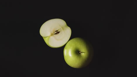 Foto-De-Estudio-Superior-De-Manzana-Verde-Entera-Y-Partida-En-Dos-Girando-Sobre-Fondo-Negro