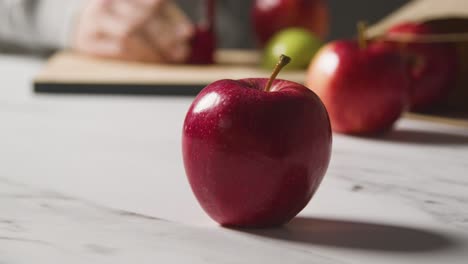 Close-Up-Of-Man-Slicing-Red-Apples-From-Paper-Bag-Of-Red-Apples-On-Marble-Kitchen-Surface