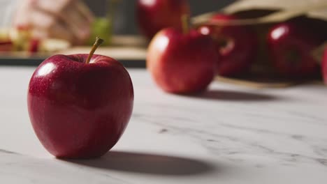 Nahaufnahme-Eines-Mannes,-Der-Rote-Äpfel-Aus-Einer-Papiertüte-Mit-Roten-Äpfeln-Auf-Einer-Marmorküchenfläche-Schneidet-1