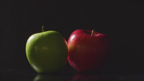 Studio-Shot-Of-Hand-Choosing-Between-Red-And-Green-Apples-Revolving-Against-Black-Background